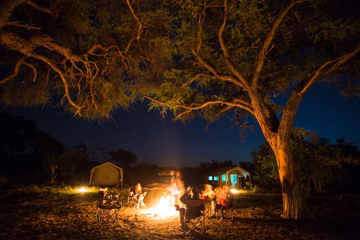 People sitting around a campfire at night during a safari photography trip