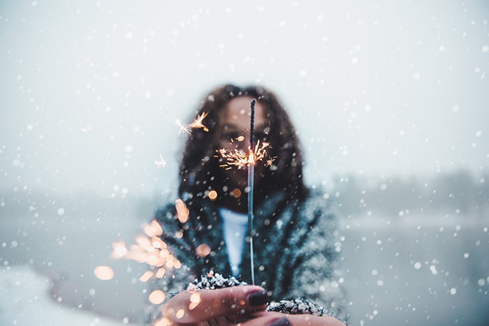 Atmospher winter portrait of a female model posing with sparklers under falling snow at night
