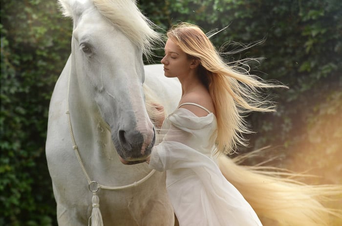 A dreamy photo of a female model with long blond hair posing beside a white horse after using Photoshop overlays