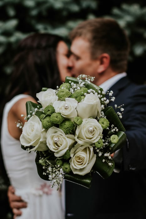 Artistic portrait of a newlywed couple holding a bouquet of flowers towards the camera - fine art wedding photography
