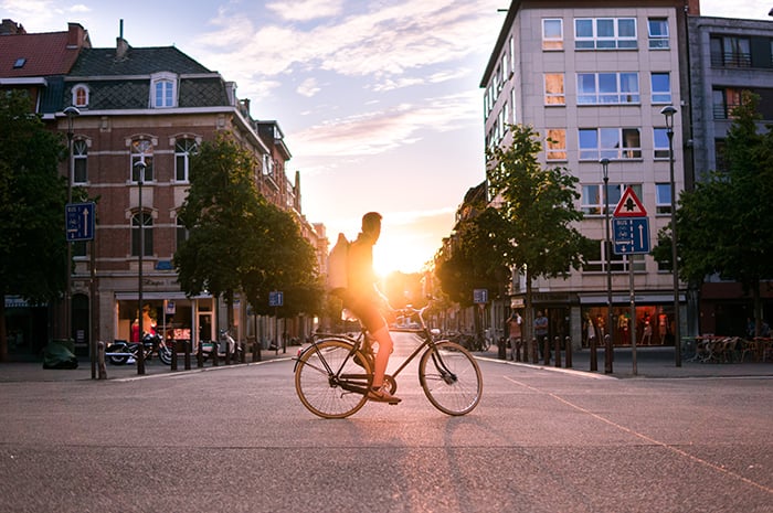 A lifestyle portrait of a man resting on a bicycle outdoors at sunset