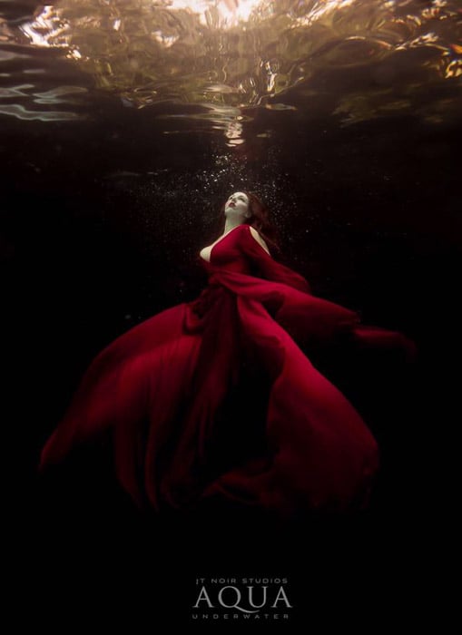 Atmospheric underwater photoshoot of a female model in a red dress posing underwater