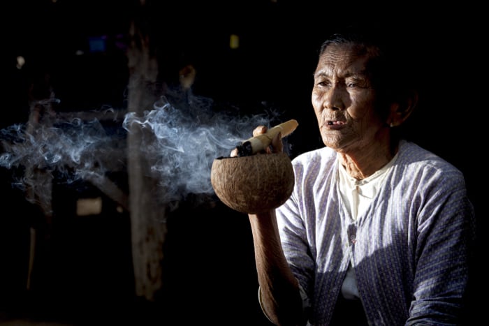 a low key portrait of an old woman smoking shot used a flash to the left of the camera