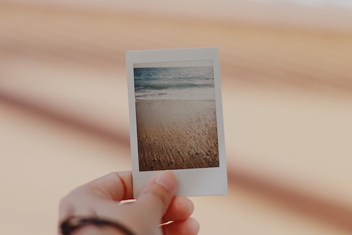 A persons holding an instant photo of a beach scene
