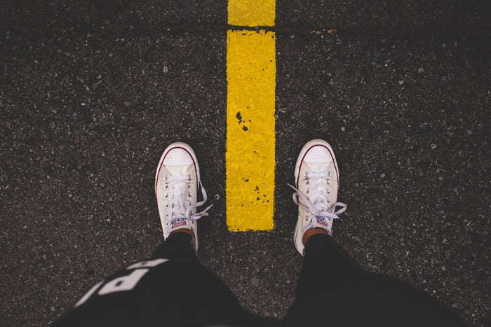 An overhead shot of a persons feet standingover a yellow line on the road