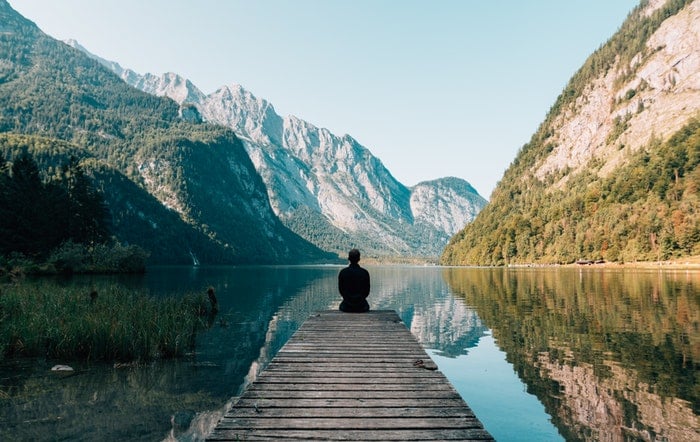 a lone figure sitting on a wooden pier by a lake, utilizing dynamic range in photography