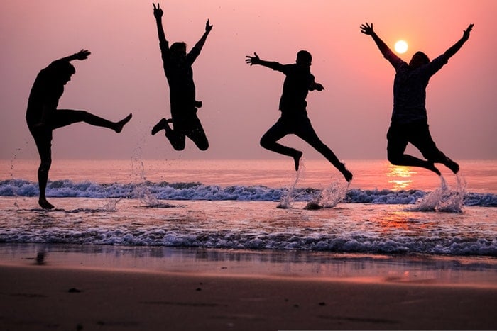 the silhouettes of four people jumping with joy on a beach at sunset, utilizing dynamic range in photography