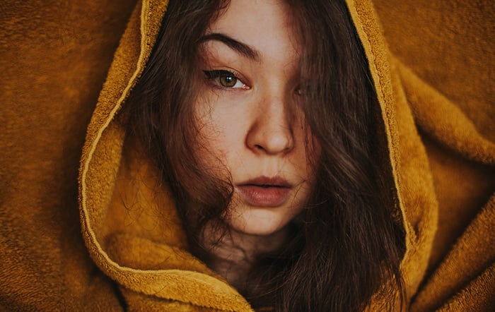 A person with long hair is wearing a beige hoodie, looking directly at the camera.