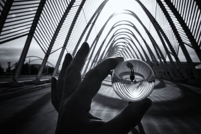 a hand holding a small lensball reflecting a black and white street photo 
