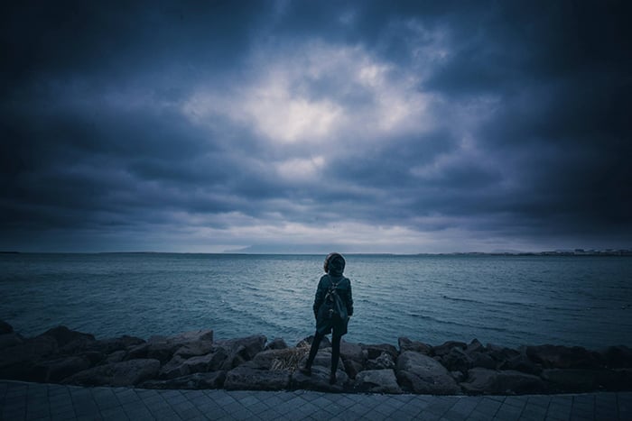 A person standing in front of a lake with dark skies