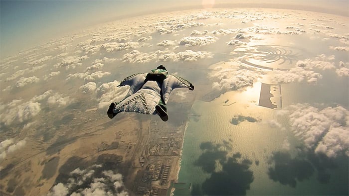 A man flying in a skydiving suit above the clouds