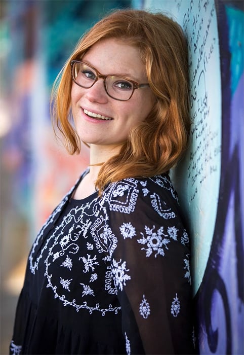 Portrait of a woman with glasses smiling and leaning against a wall 