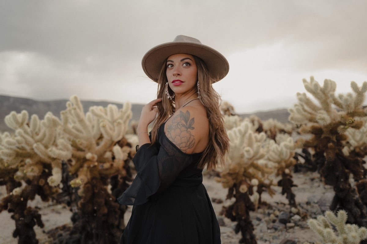 A women in a hat and sleeveless dress posing outside on a cloudy day