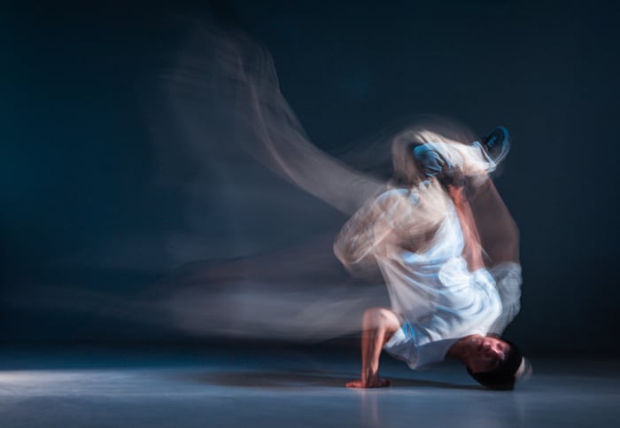 Break dancer during movement, standing on his head, with a dark background behind him.