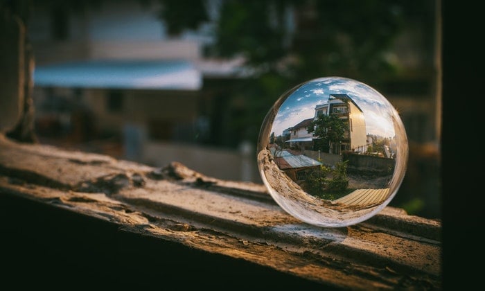 A lensball placed on a window frame with a house reflected through it