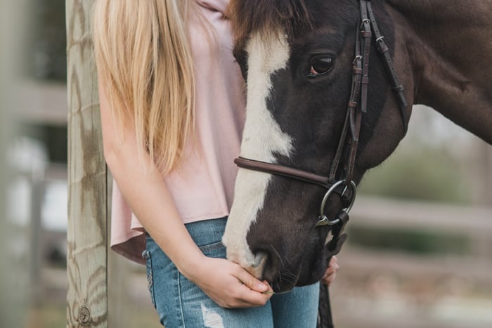 A blonde girl holding a horses bridle