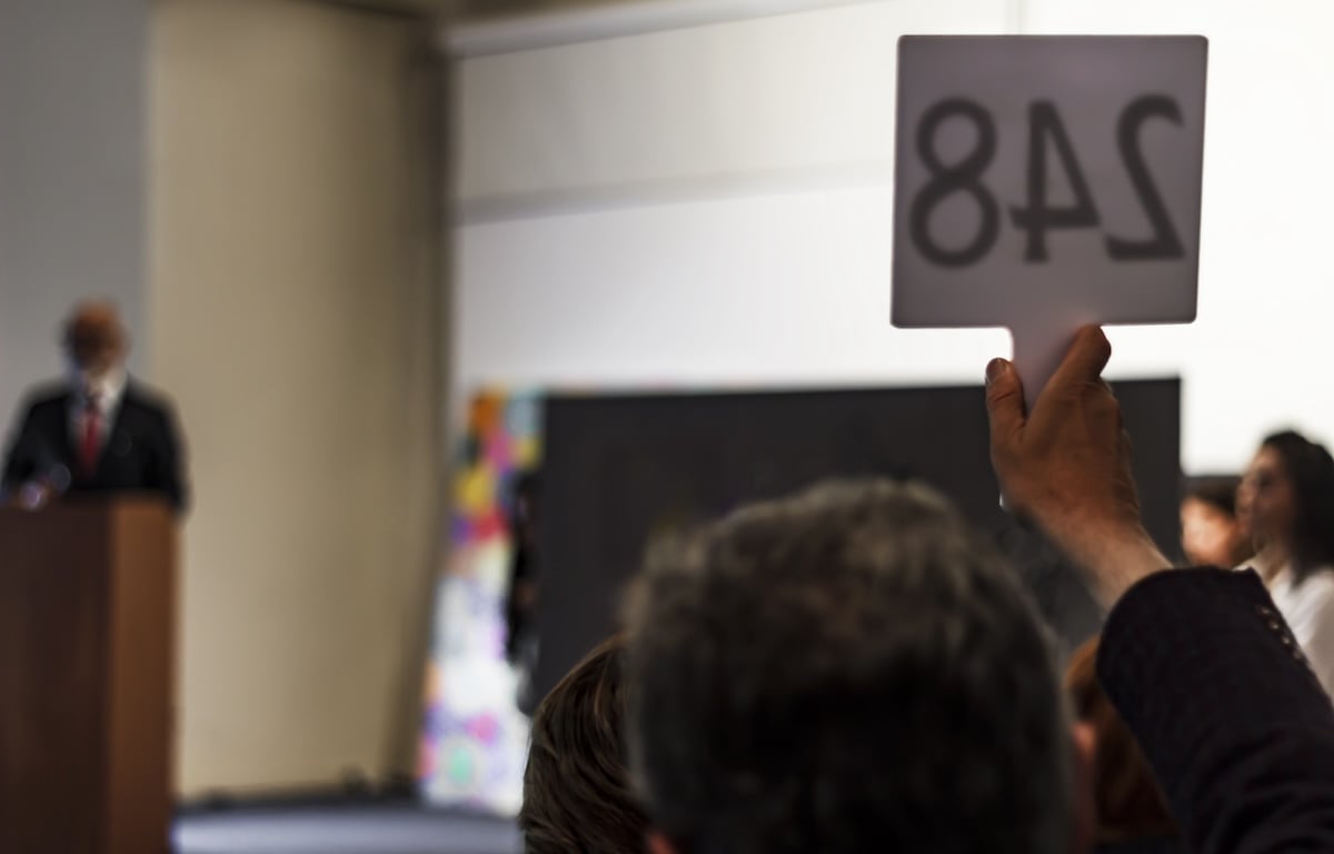 A raised hand with a number on a sign for an auction for the most expensive photographs