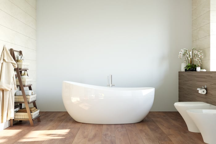 A bathroom with a white bath in the middle. Natural light coming from the window.