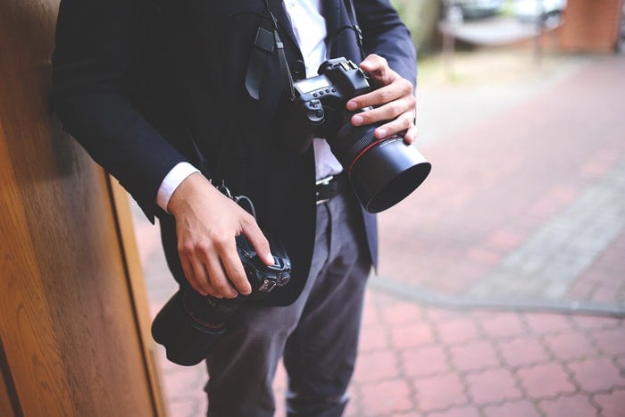 An individual standing near a doorway, holding two cameras.