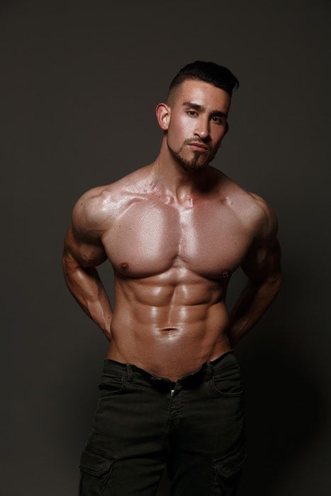Boudoir photo of a half-naked male model standing in fron of a neutral background
