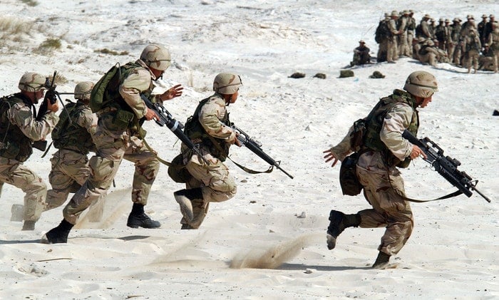a photo of military troops running in the sand