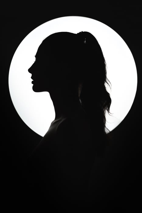 Fine art silhouette of a young woman against the round light source.