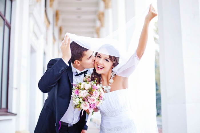 A picture of a married couple where the groom gives a kiss under the veil