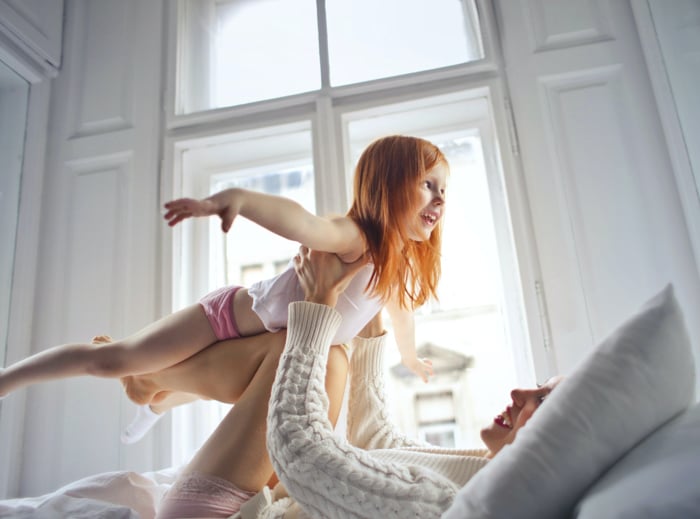 Family portraits posing of a mother lifting a young daughter in the air on bed