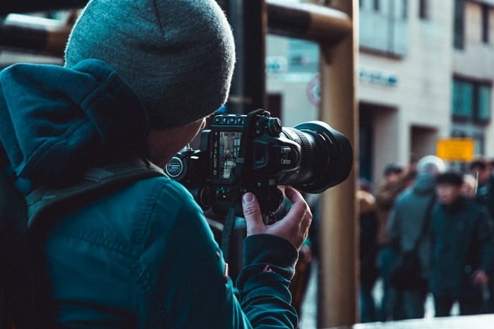 A man taking a photograph with his camera on a busy street.
