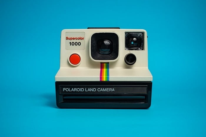 A vintage Polaroid camera with a retro design, sitting on a blue surface.