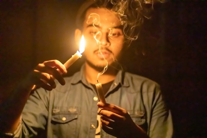 A person holding a lit candle and a candle with smoke trailing off of it