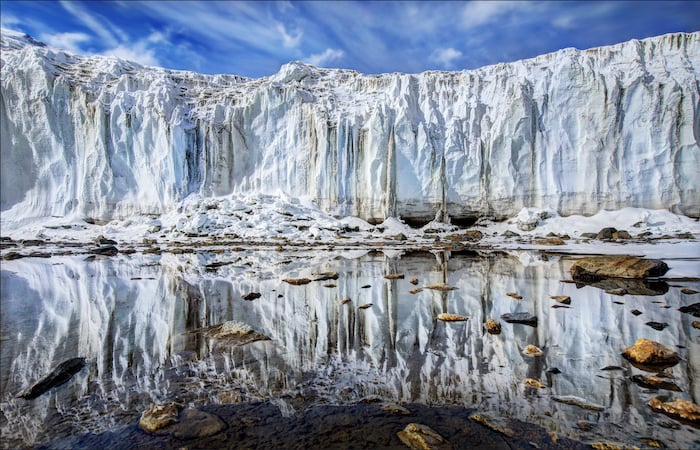impressive landscape photography: face of a glacier mirrored on still water