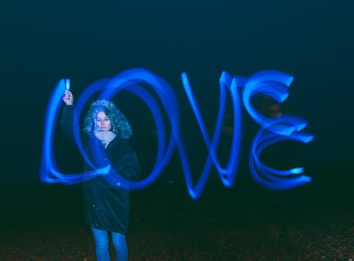 A person is holding a blue light pen that is creating the word love with their hand. 