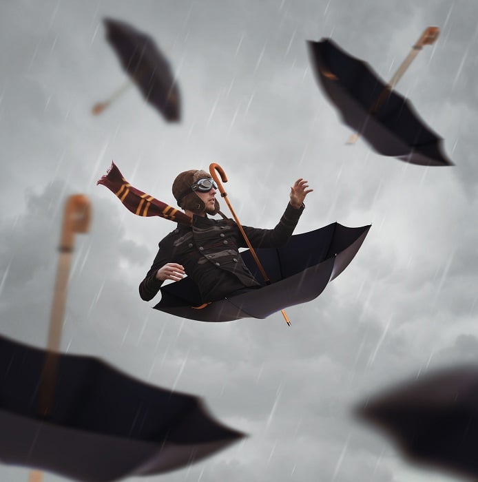 A man riding an umbrella in the rain, with multiple umbrellas falling around him.