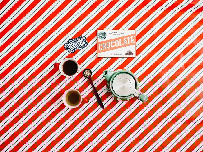 flat lay background idea: tea and chocolates on top of Christmas themed wrapping paper