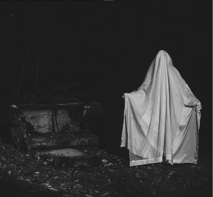 Photo of a person dressed as a ghost by a filthy outdoor sofa