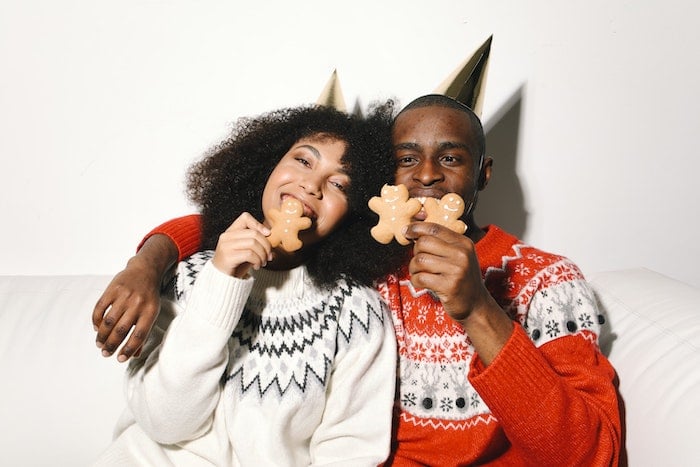 A couple in holiday sweaters taking a bite of gingerbread cookies for Christmas card photo ideas