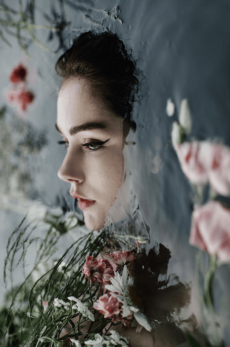 A woman's face above water surrounded by flowers and foliage