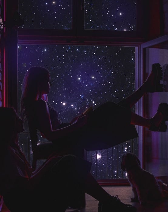 Composite image of a girl and dog sitting by a window in the night sky
