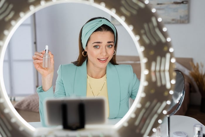 Woman holding up a bottle of makeup seen through a ring light