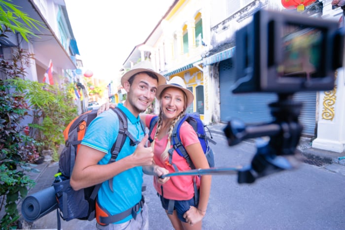 Young backpacking couple take a selfie on the street with an action camera and selfie stick Young backpacking couple take a selfie on the street with an action camera and selfie stick