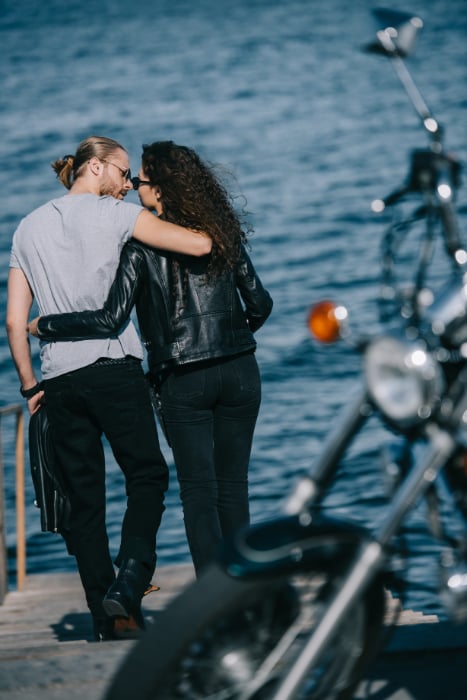 Couple by the sea, arms around each other, with their motorbike in the foreground Couple by the sea, arms around each other, with their motorbike in the foreground