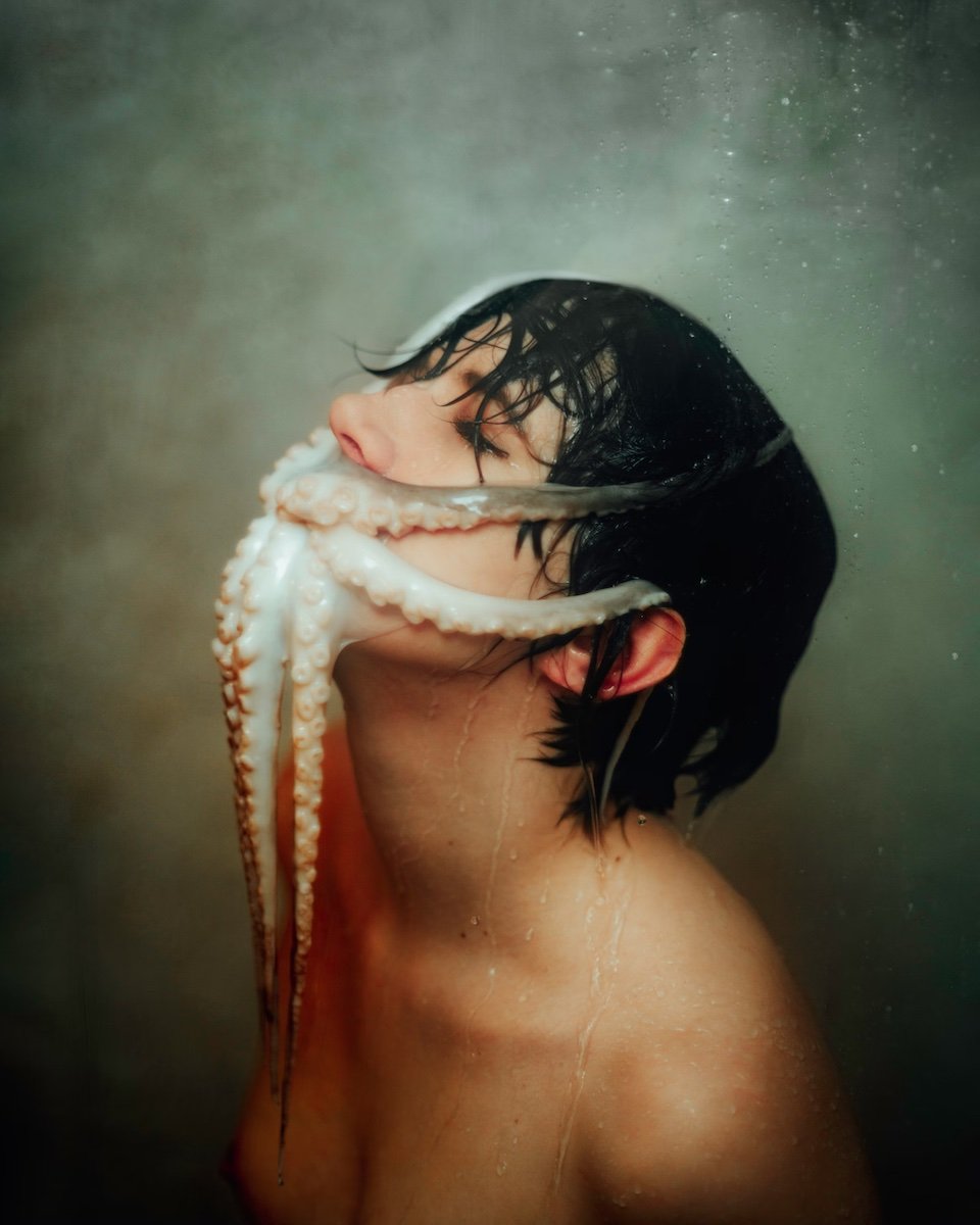 A shirtless man looking up with a octopus on his face