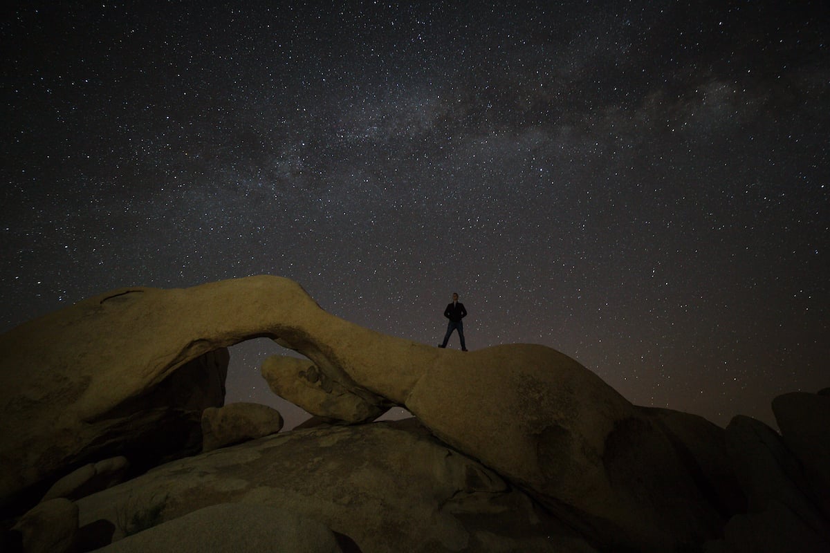 RAW nighttime image of a person standing on a desert formation under the stars