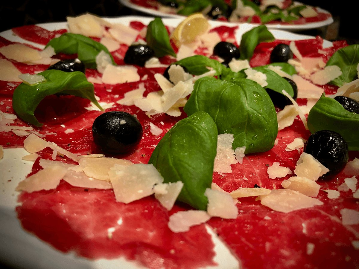 A close-up of beef carpaccio, fresh basil and parmesan cheese