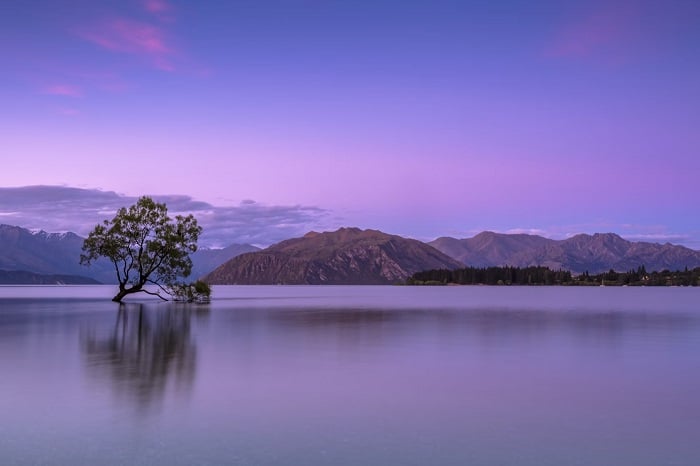 Landscape image of a lake with mountains in the background and a purple sky