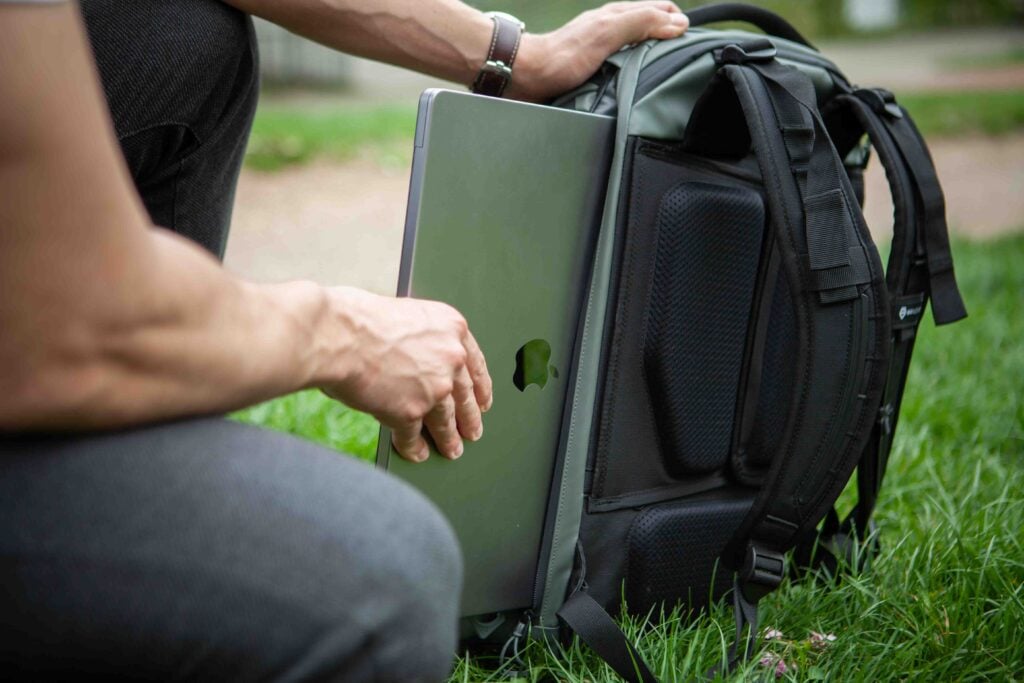 A man is seated on the ground, holding a laptop computer.