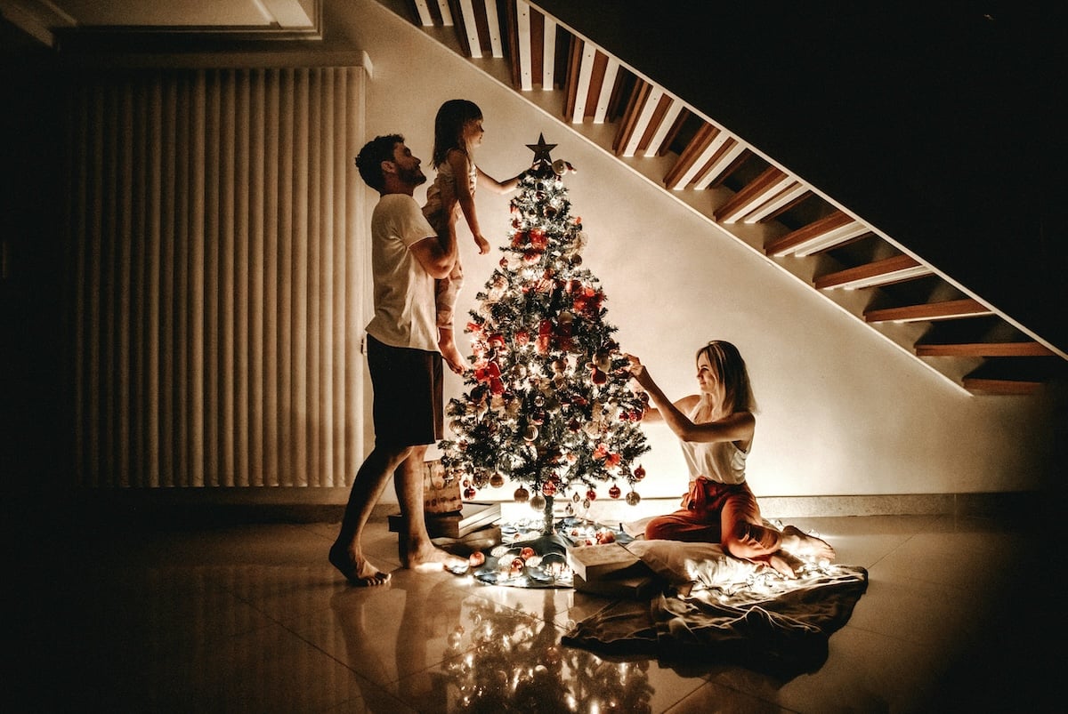 A family of three is gathered around a Christmas tree, decorated in a festive manner.