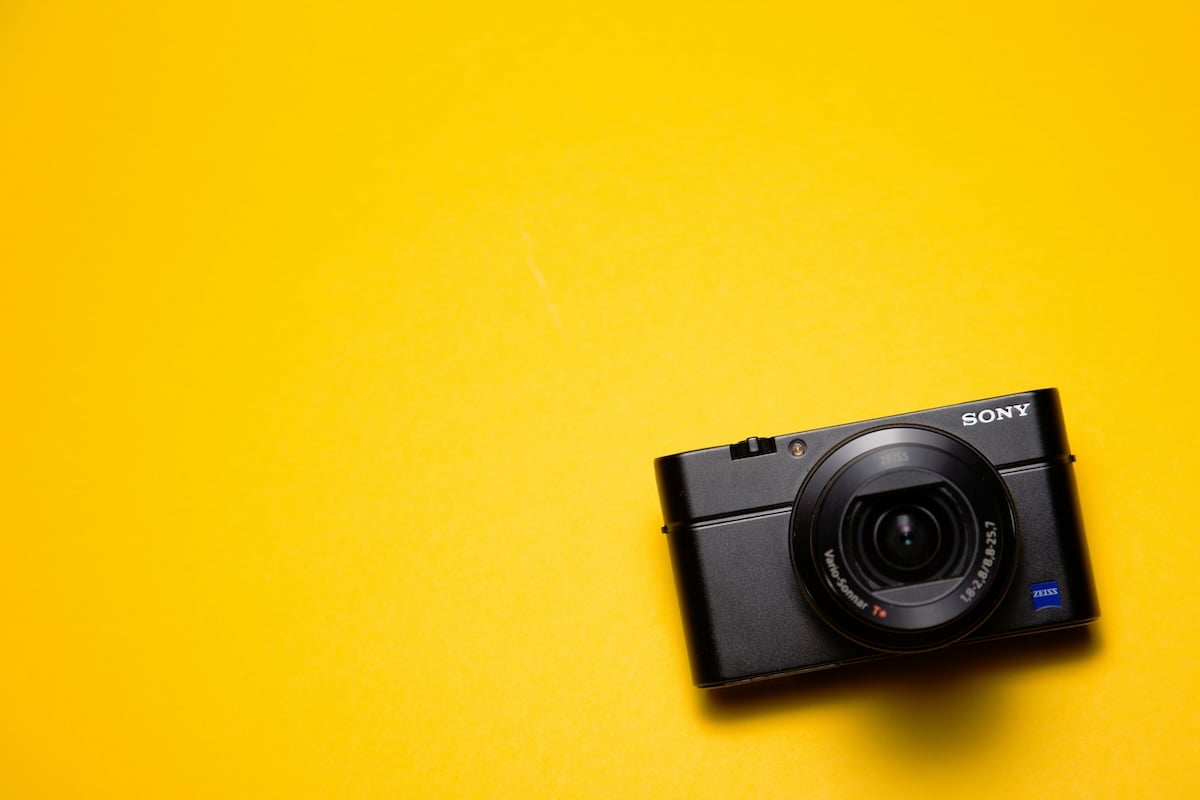  A small, black digital camera sits on a bright yellow surface. 
