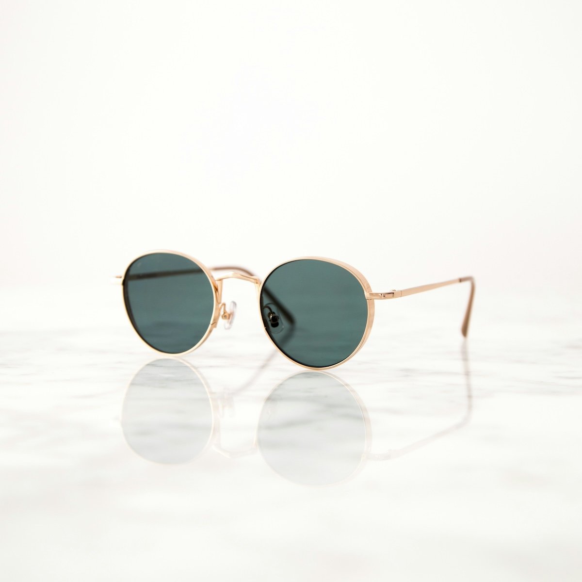 A pair of rose gold sunglasses with dark blue lenses resting on a reflective surface, possibly a marble table. 